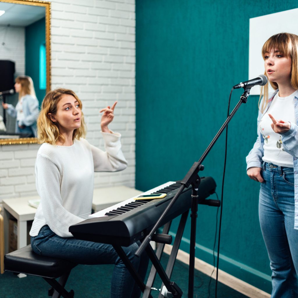 Vocal teacher showing her student how to sing in the microphone
