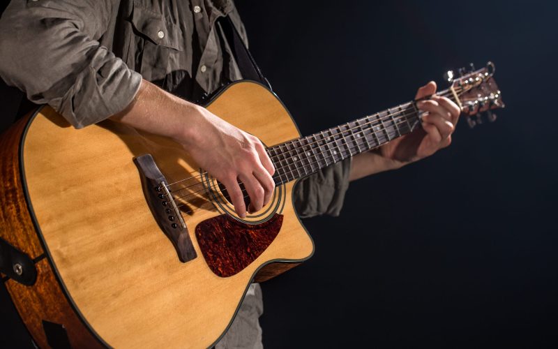 Guitarist, music. A young man plays an acoustic guitar on a black isolated background. Pointed light