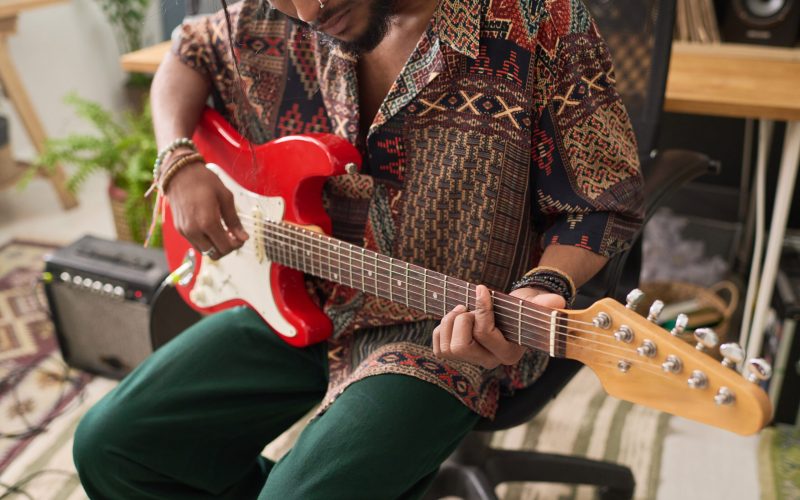 Cropped shot of young talented musician in stylish casualwear playing bass guitar in home studio before recording his new music