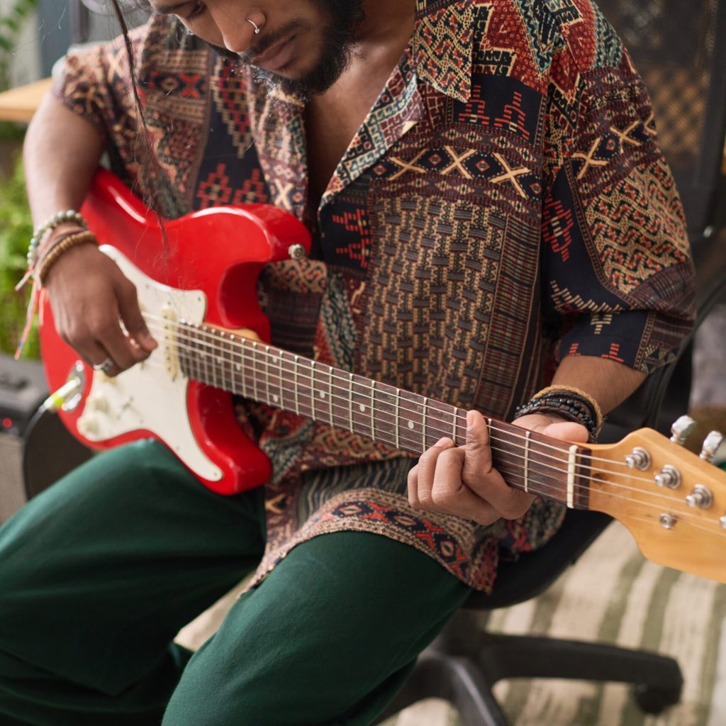 Cropped shot of young talented musician in stylish casualwear playing bass guitar in home studio before recording his new music