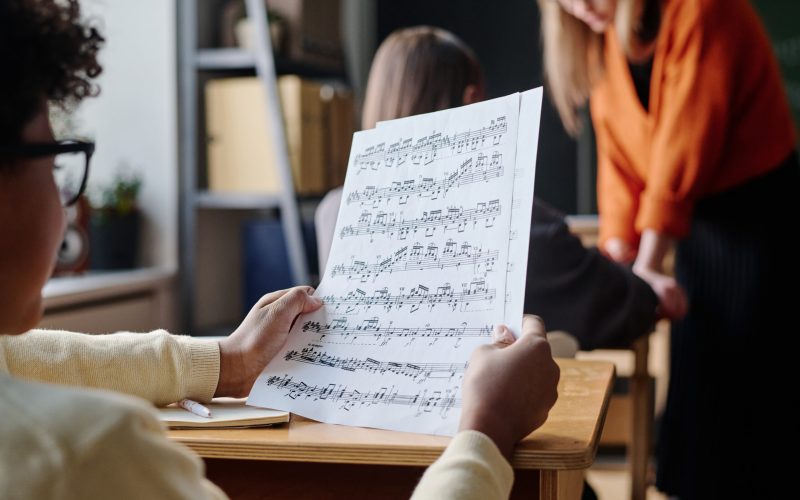 Selective focus shot of unrecognizable African American boy sitting at desk in classroom looking through sheet music paper during lesson